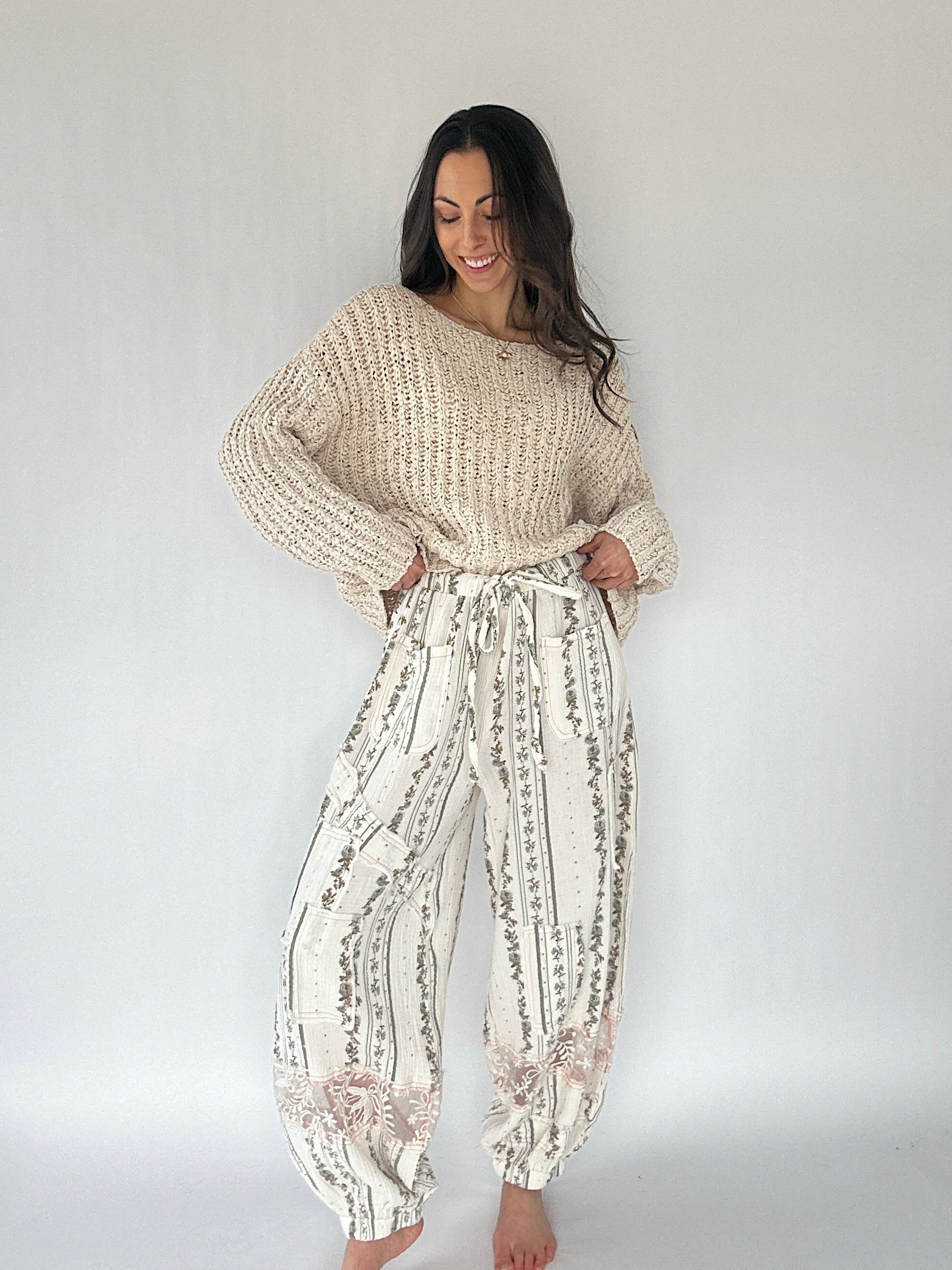 Woman wearing a beige knit sweater and patterned pants against a white background