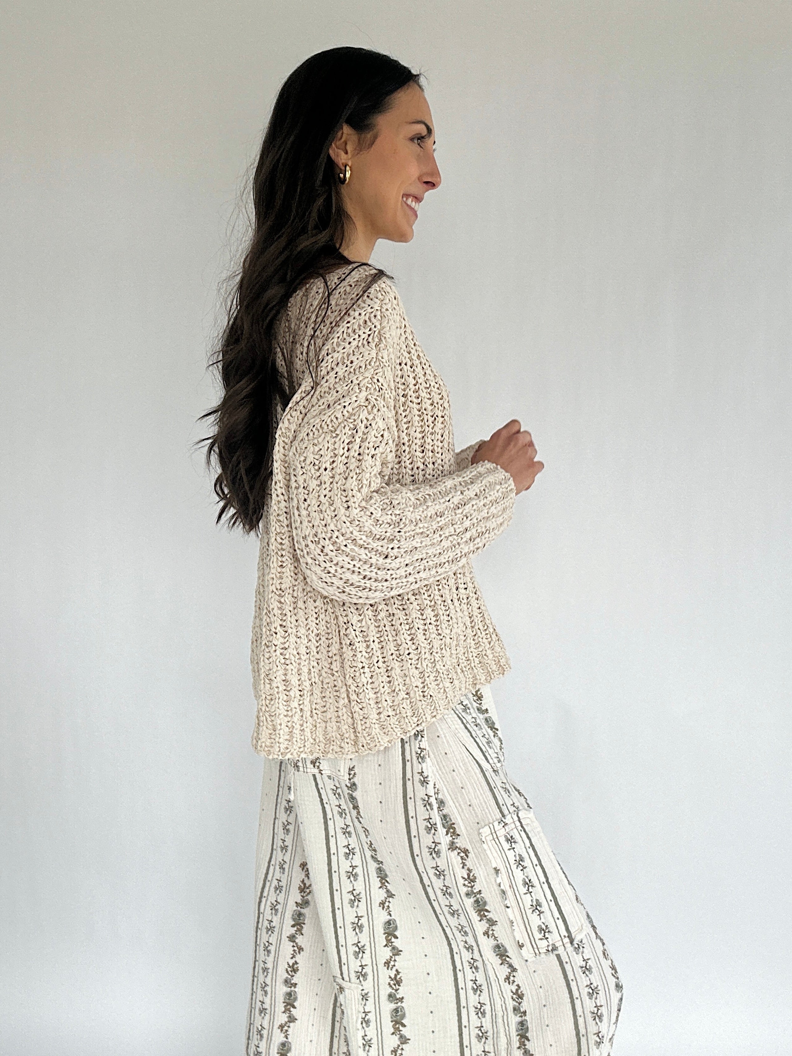Woman wearing a beige knitted sweater and patterned pants against a white background from side