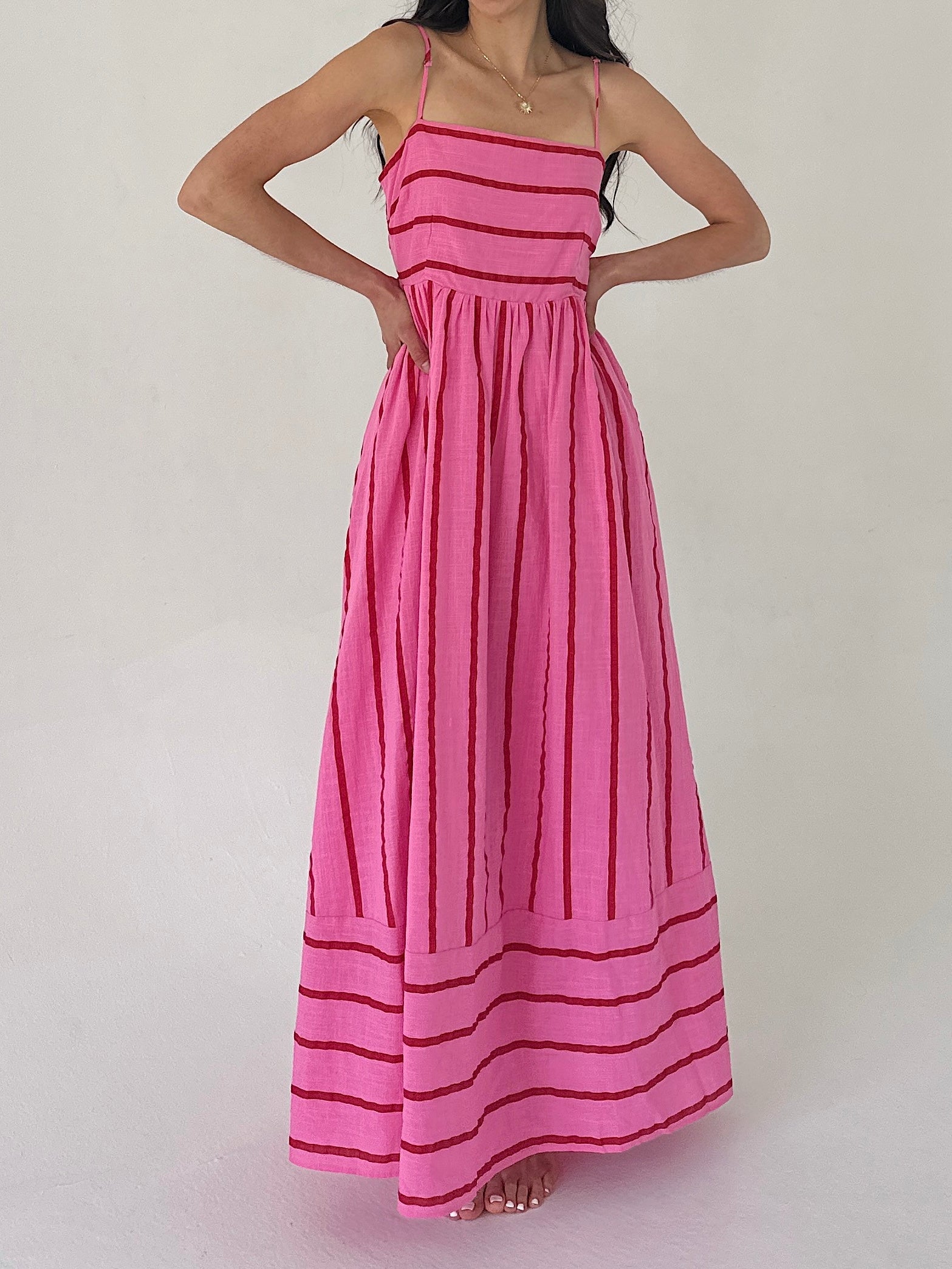 Woman wearing a pink dress with red stripes on a plain background
