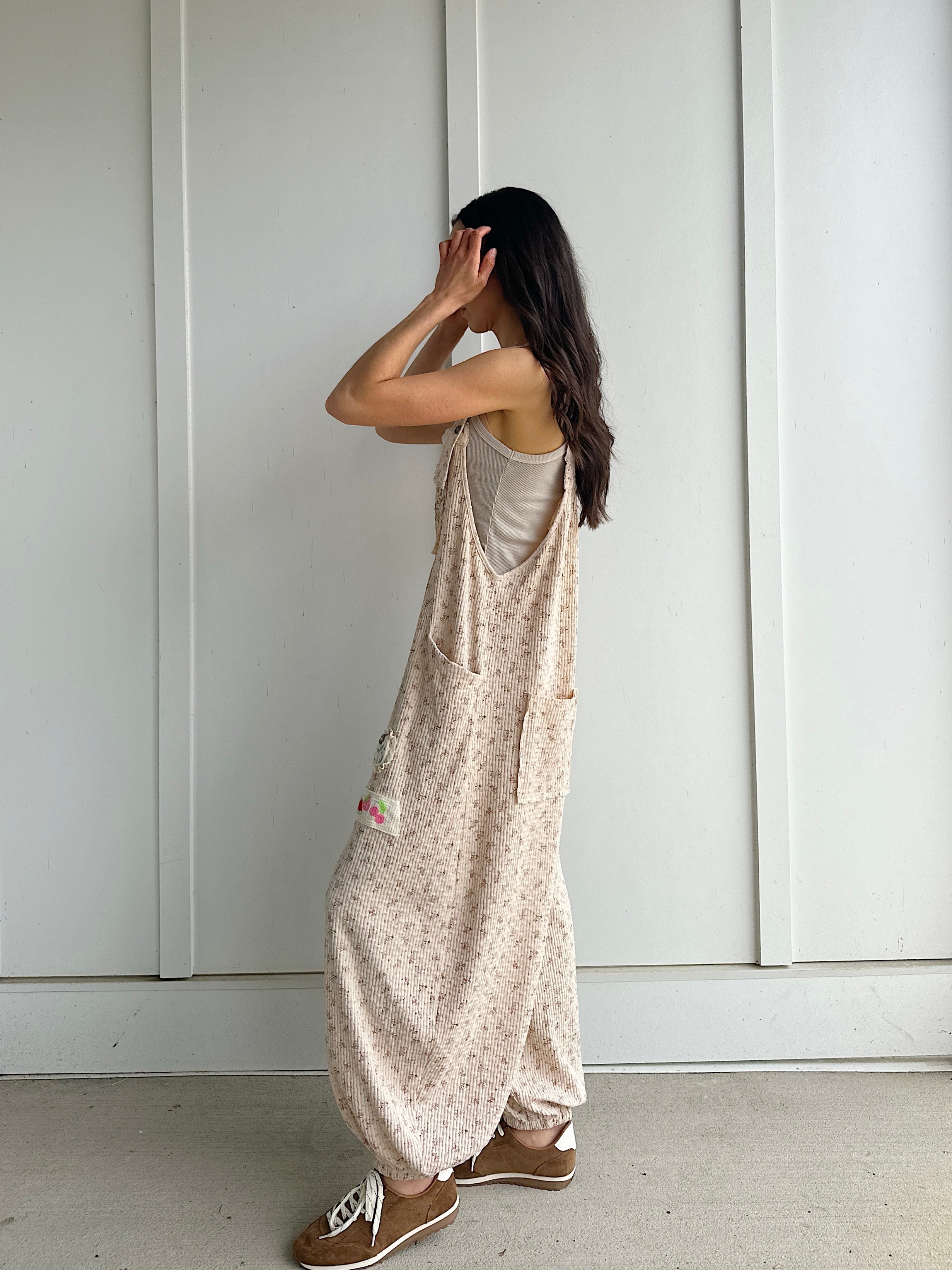 Person wearing a beige patterned overalls standing against a white paneled wall showing side view
