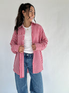 Woman wearing a red and white checkered shirt over a white top and blue jeans on a plain background