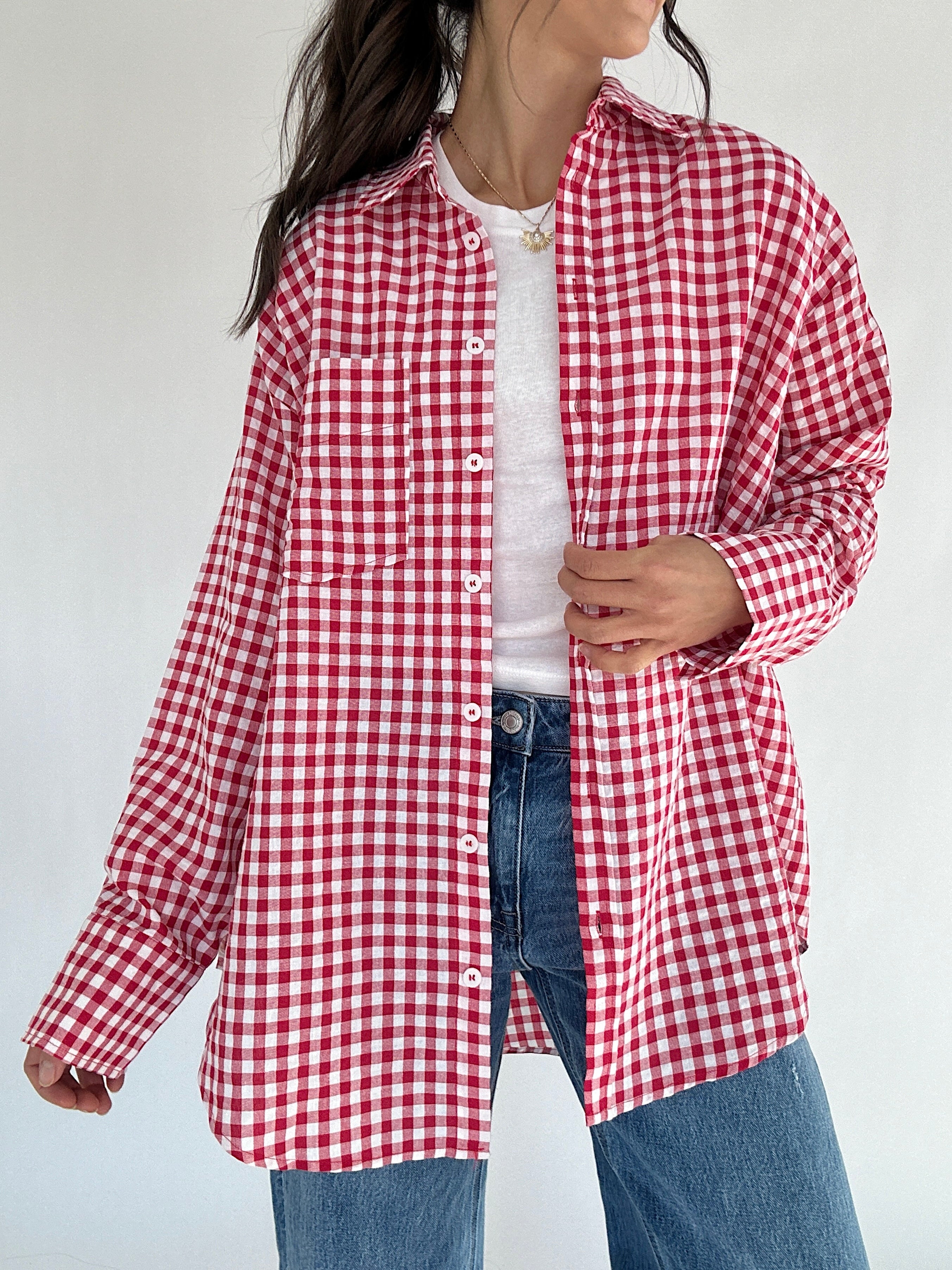 Person wearing a red and white checkered shirt over a white top with blue jeans on a plain background