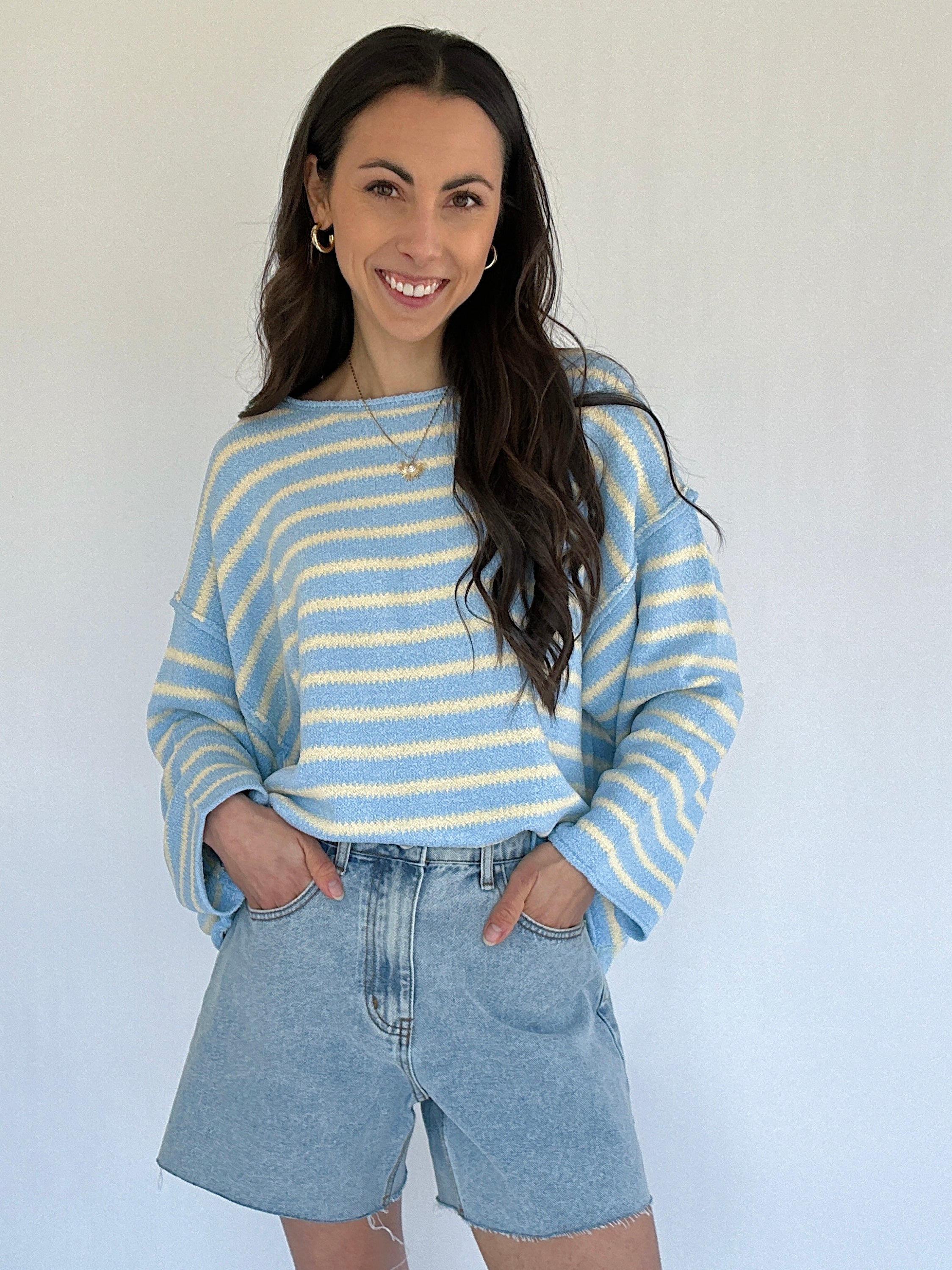 Woman wearing a blue and white striped sweater and denim shorts against a white background