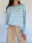 Person wearing a blue and yellow striped sweater with floral pants against a plain background