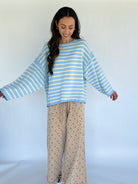 Woman wearing a blue and yellow striped sweater and patterned pants on a white background