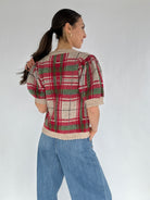 Woman wearing a plaid short sleeve sweater and jeans against a plain background back view