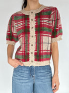 Person wearing a plaid cardigan top with red, green, and beige colors on a white background