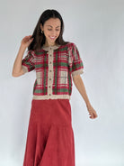 Woman wearing a red plaid sweater top and red skirt against a white background
