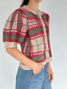 Person wearing a plaid cardigan sweater top with puffed sleeves on a plain background