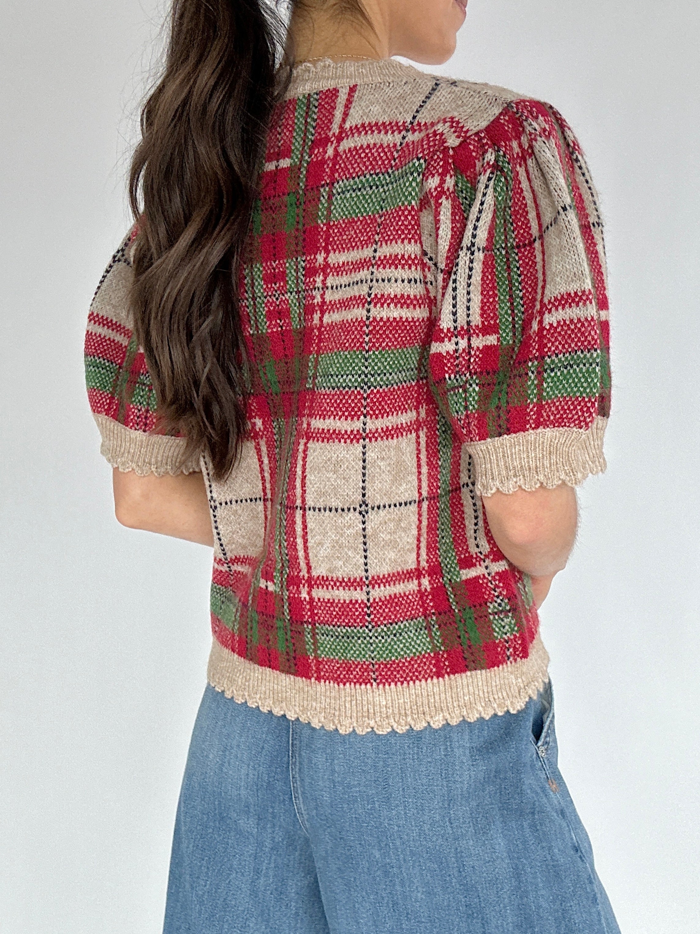 Person wearing a plaid short sleeve sweater with a white background from back