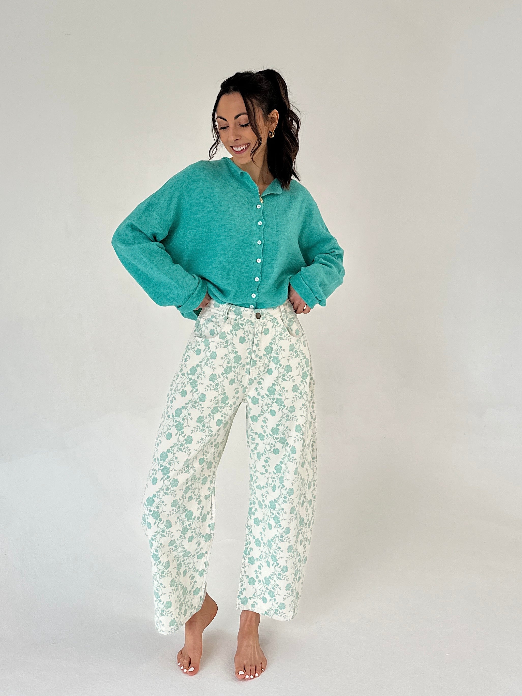 Woman wearing a teal sweater and floral pants on a white background