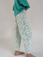 Person wearing teal floral pants and a green sweater on a plain background from side