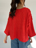 Person wearing a bright coral cable knit sweater with a plain background showing the back