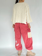 Person wearing a cream sweater and red cargo pants on a plain background back view