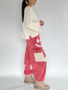 Person wearing a cream sweater and red pants with a white background side view