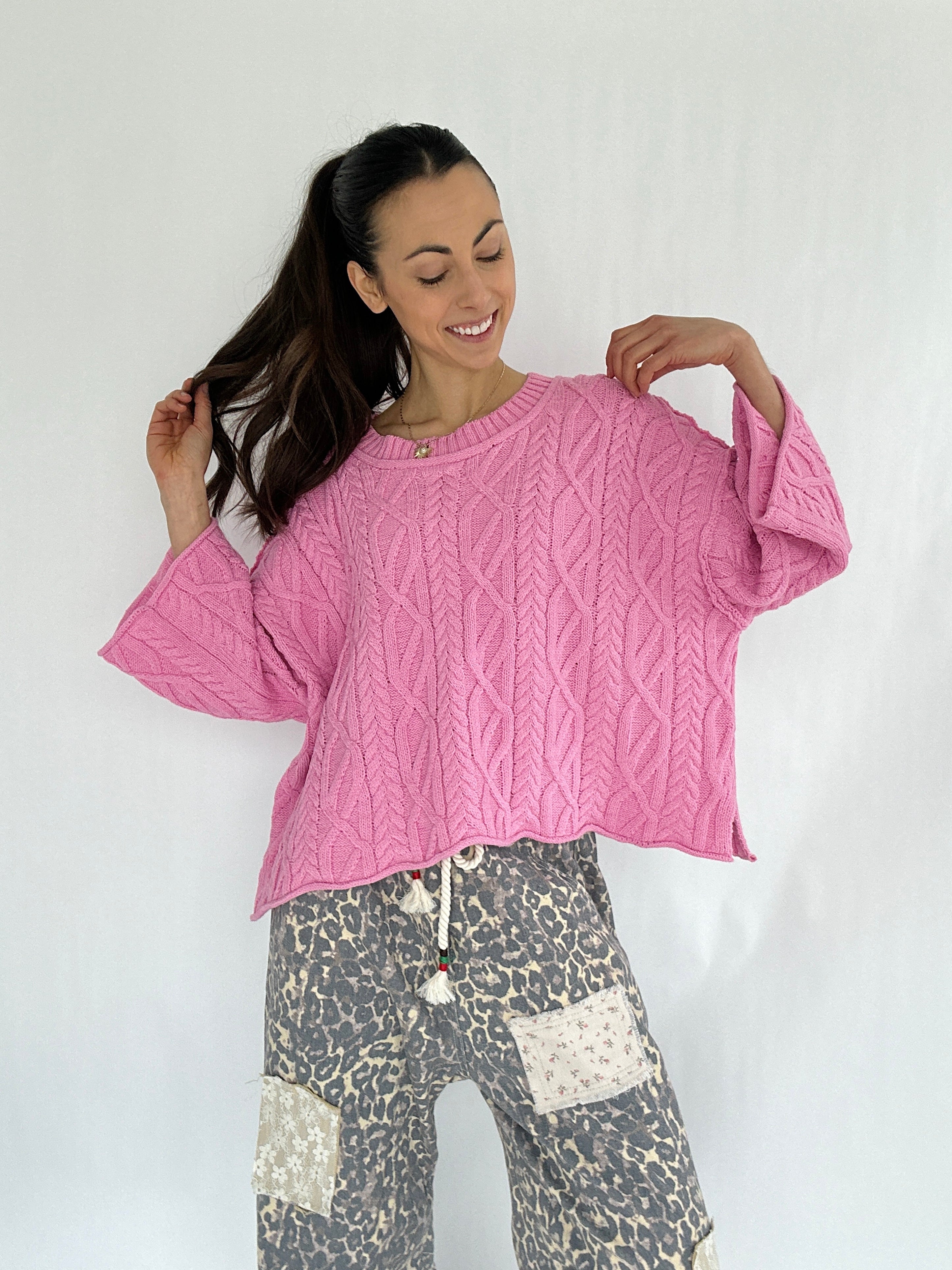 Woman wearing a pink cable knit sweater and patterned pants on a white background