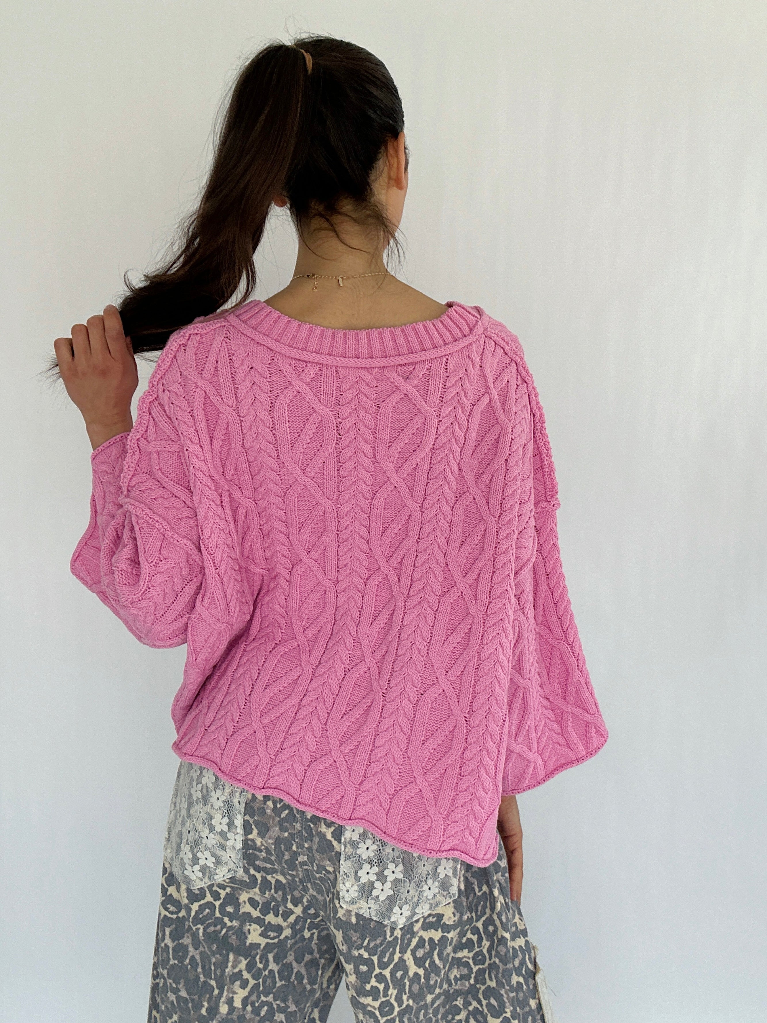 Person wearing a pink knitted sweater with a white background showing the back
