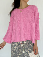 Person wearing a pink cable knit sweater with a white background