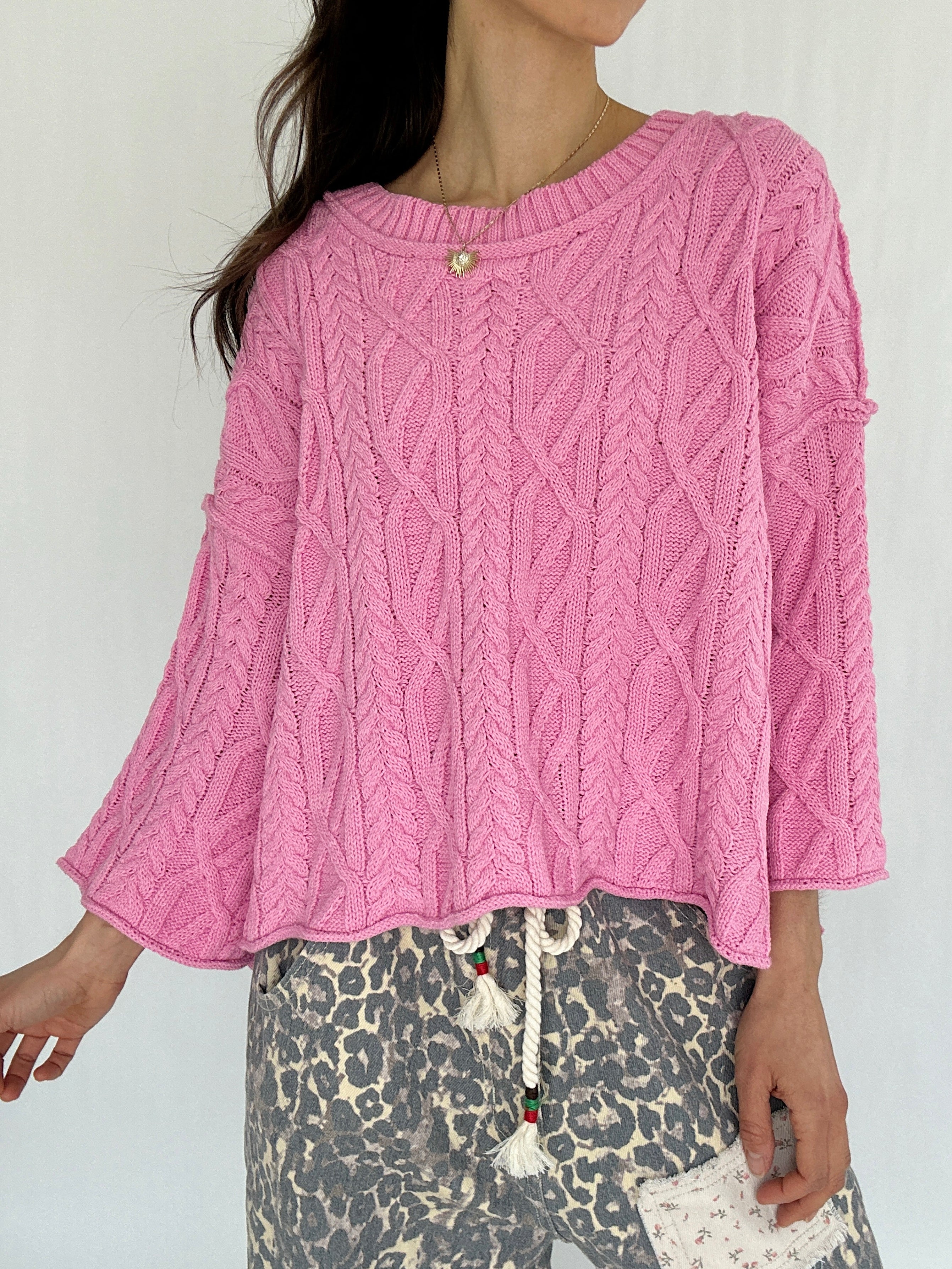 Person wearing a pink cable knit sweater with a white background