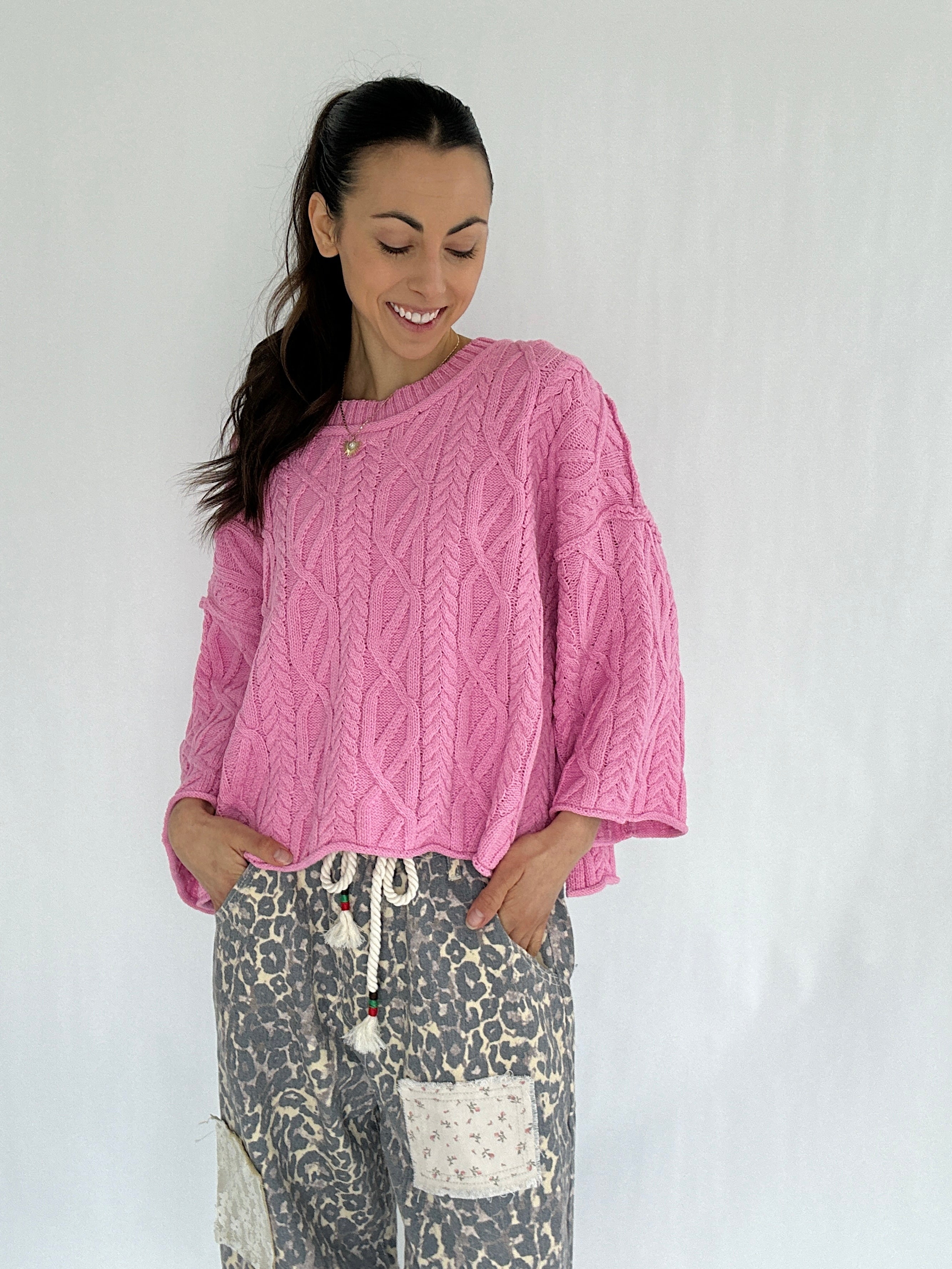 Woman wearing a pink cable knit sweater and patterned pants on a white background