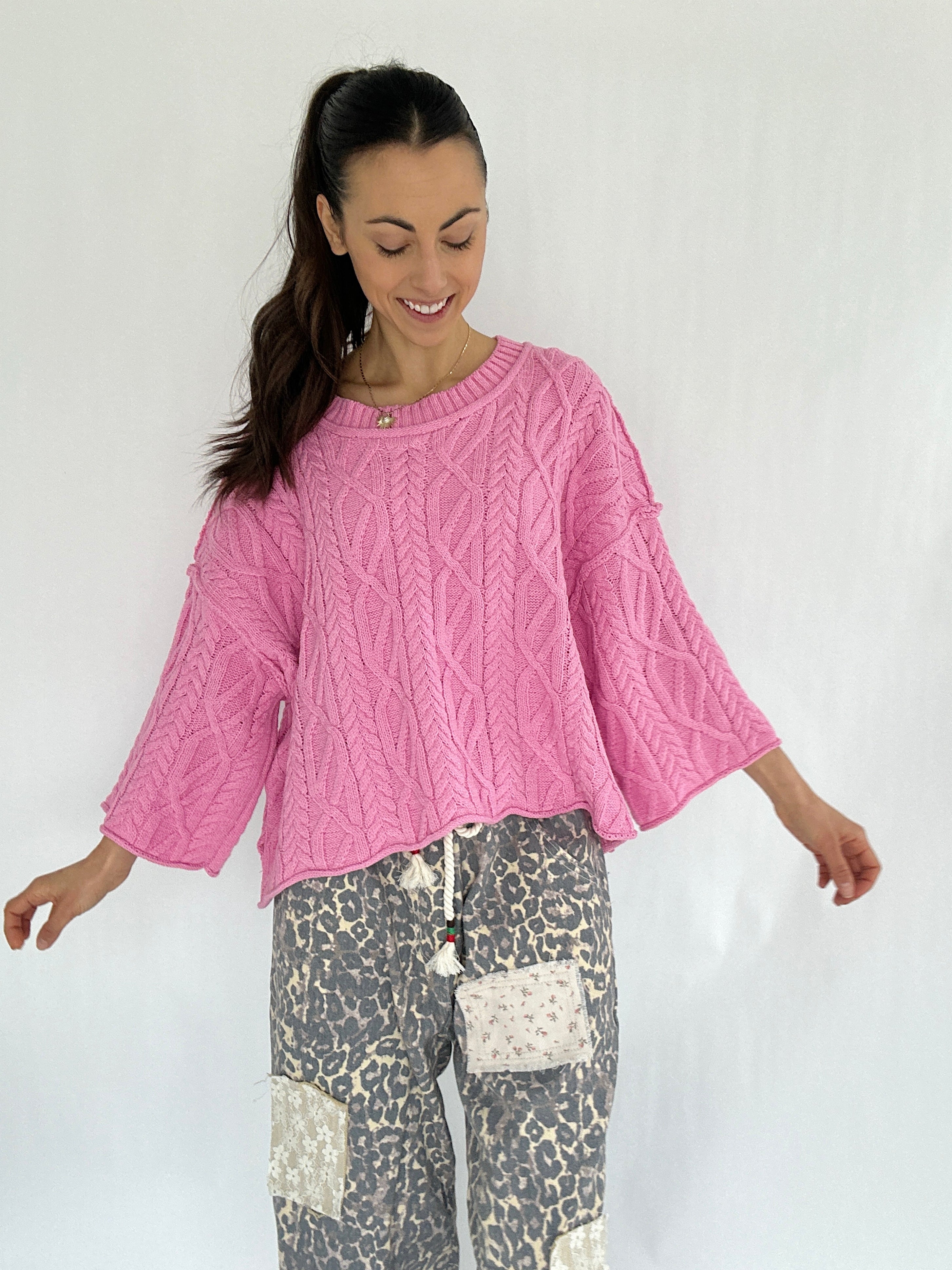 Woman wearing a pink cable knit sweater and leopard patterned pants on a white background