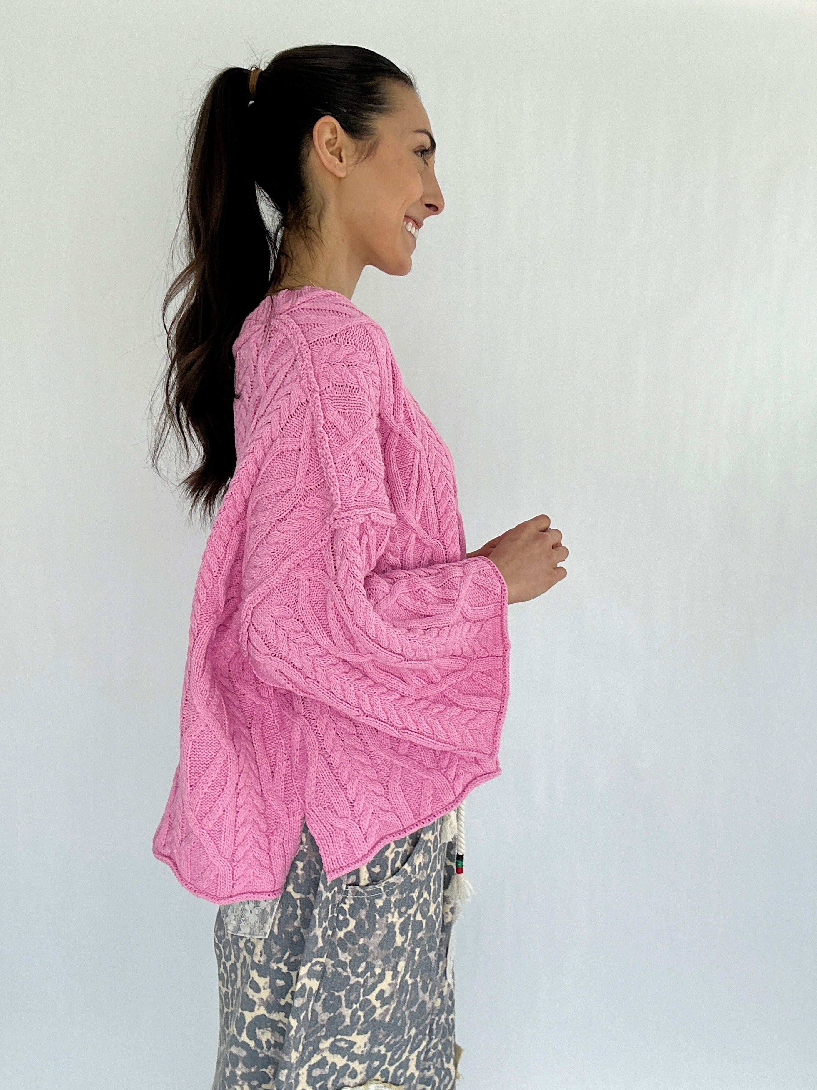 Woman wearing a pink knitted sweater against a white background showing side profile