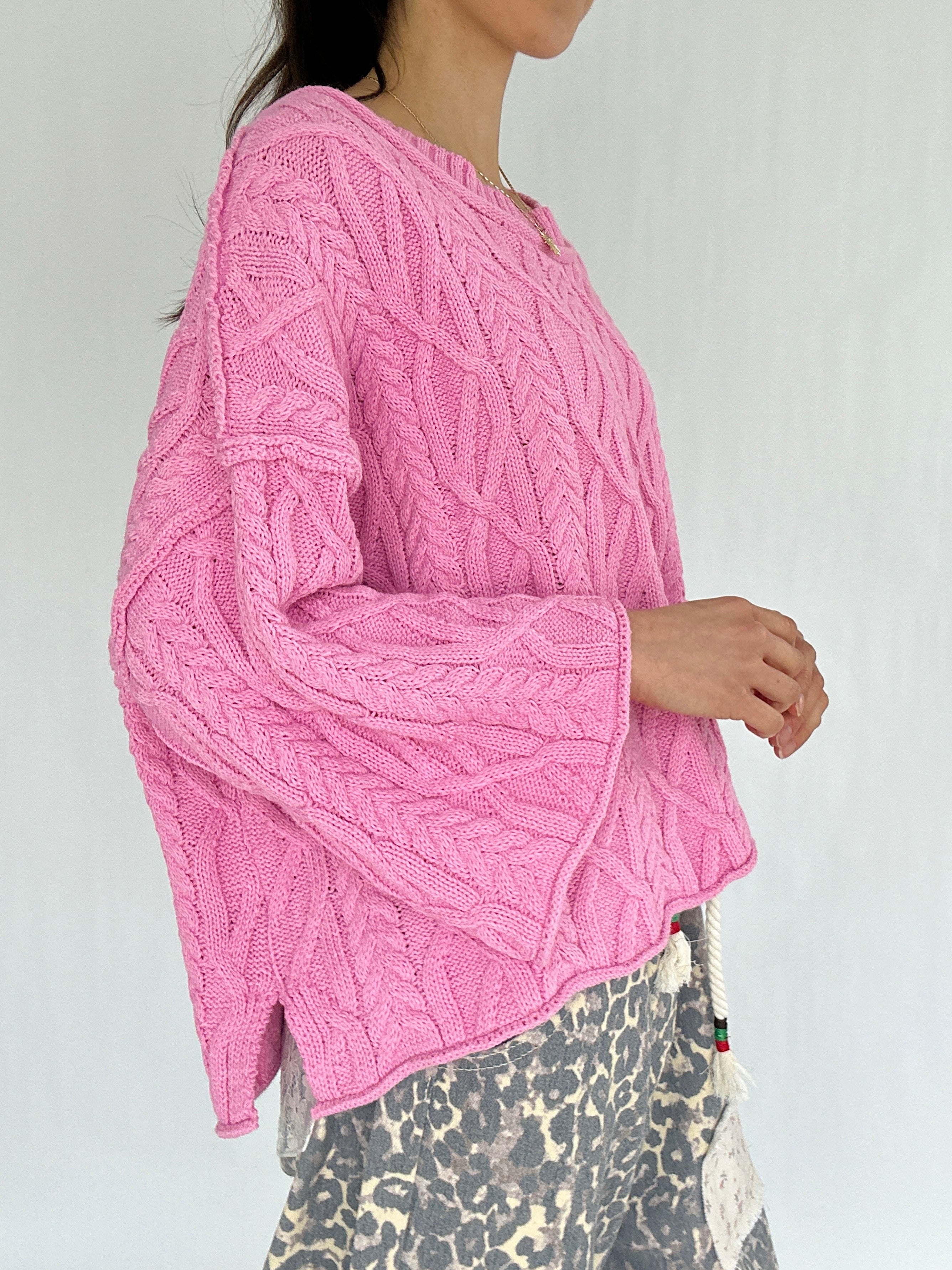 Person wearing a pink knitted sweater with a white background showing up close side 