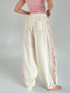 Person wearing cream-colored pants with floral embroidery on a plain background showing back pocket details