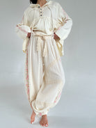 Person wearing a cream-colored outfit with lace details on a plain background
