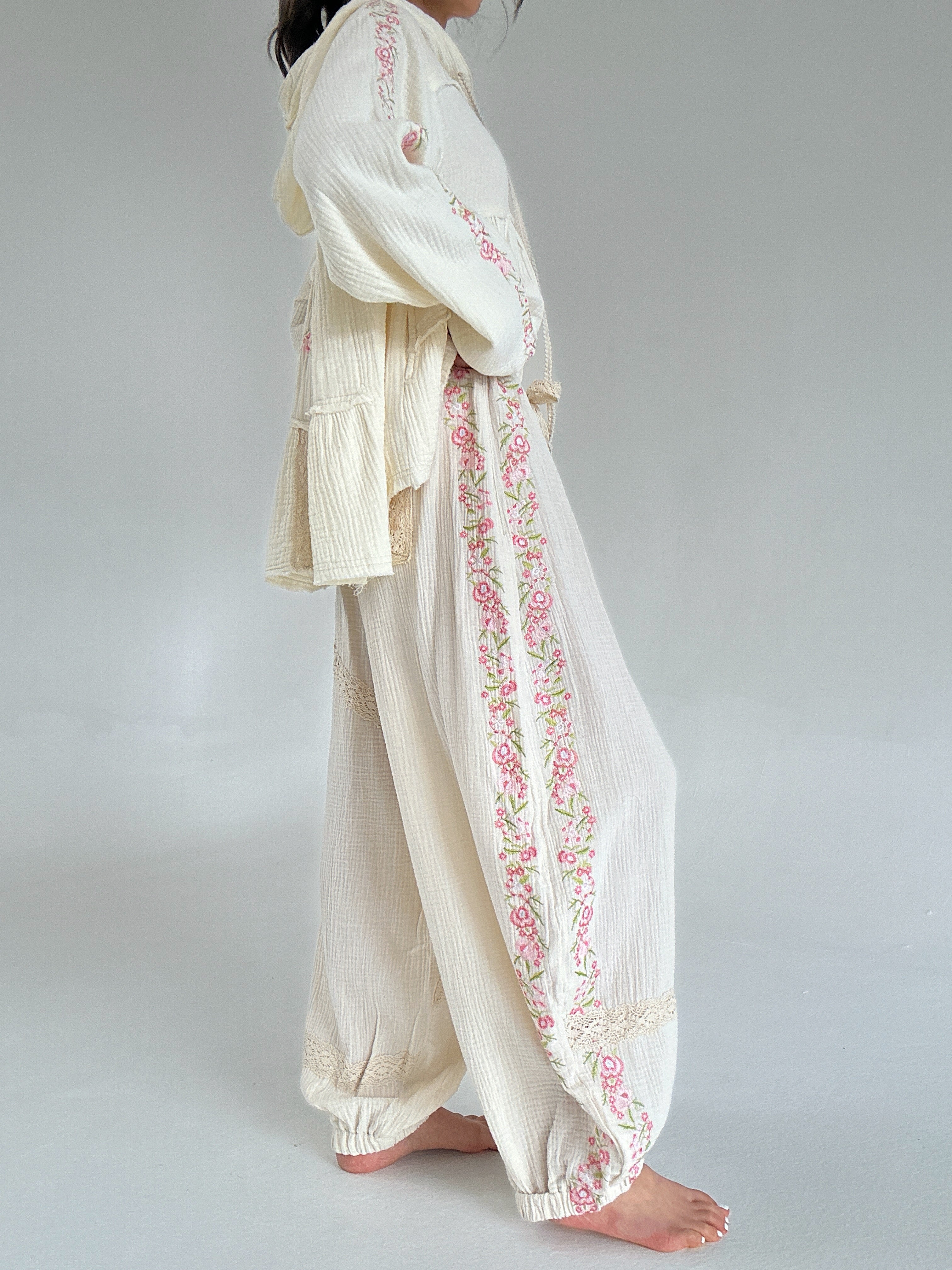 Person wearing a cream-colored outfit with floral embroidery on a plain background showing side embroidery