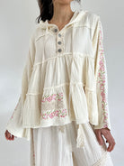 Woman wearing a cream-colored blouse with floral embroidery on a white background