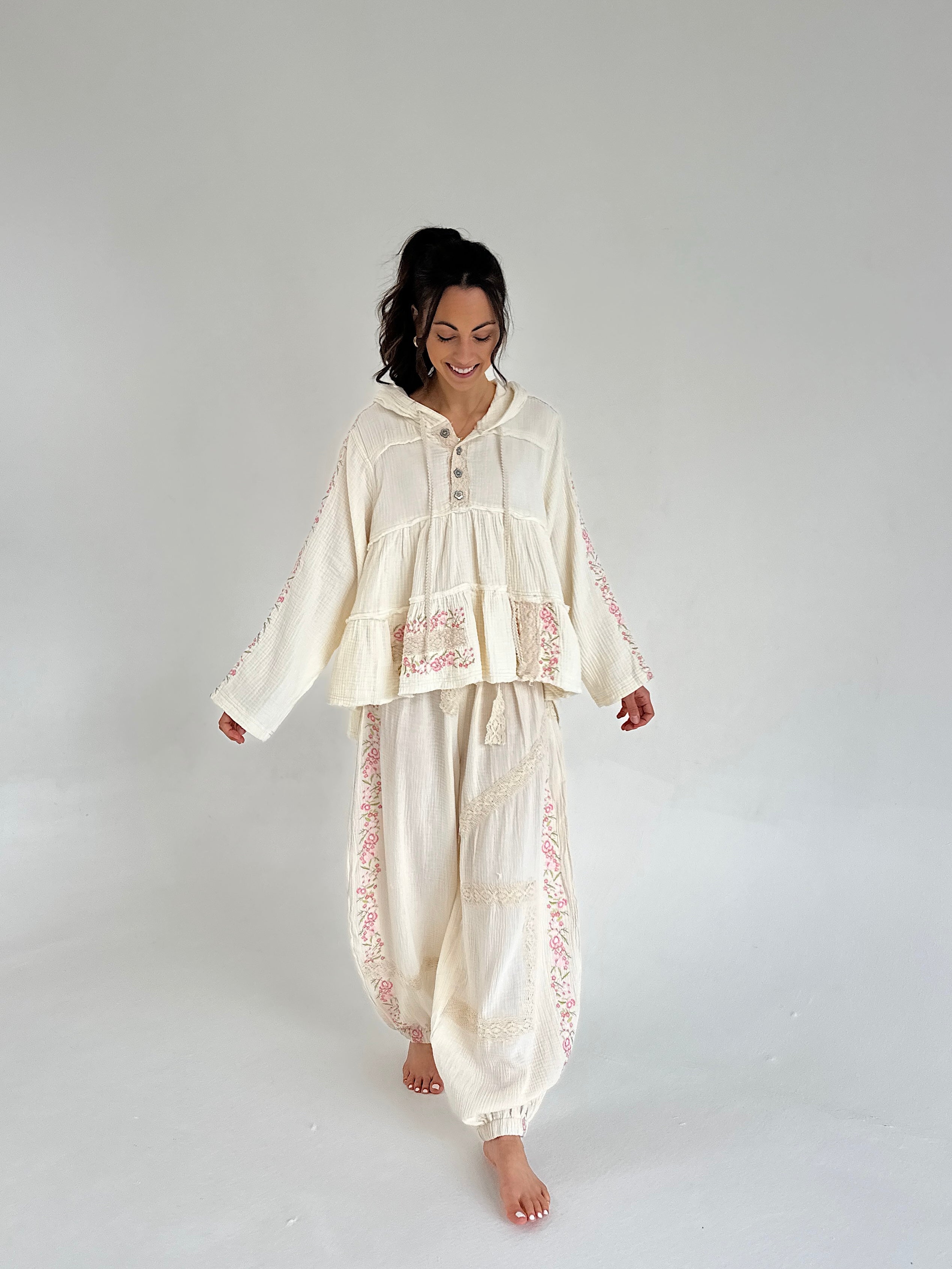 Woman wearing a cream-colored outfit with floral patterns on a plain background