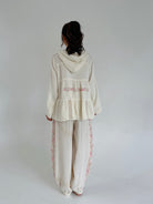 Person wearing a cream-colored outfit with floral embroidery on a plain background showing back