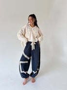 A woman stands barefoot in a studio wearing a cream lace top and matching with dark navy wide-leg pants featuring cream lace trim.
