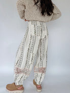 Person wearing a beige knit sweater and patterned pants on a white background from back