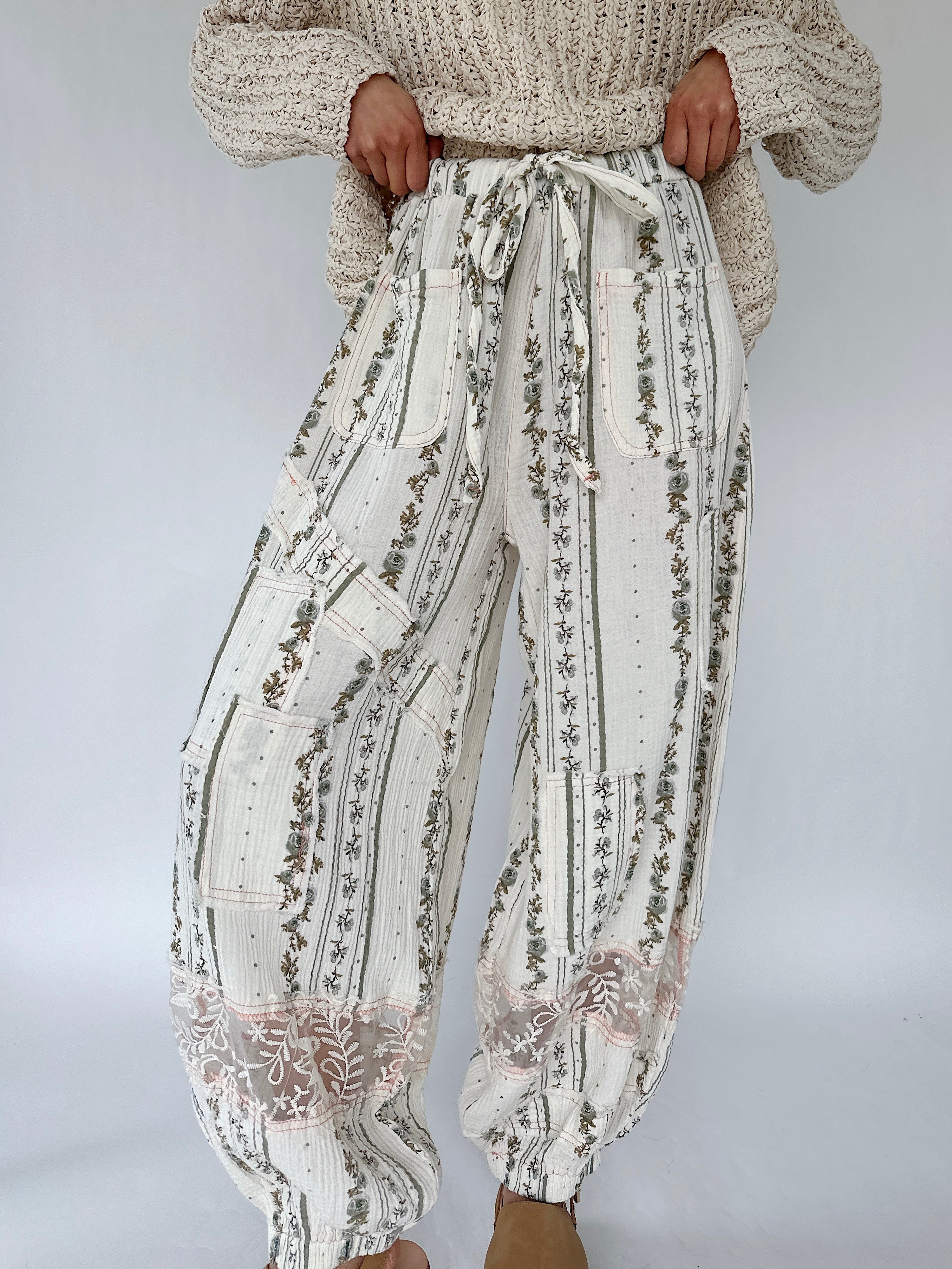 Person wearing white floral-patterned pants with drawstring waist against a plain background