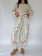 Person wearing a beige knitted sweater and patterned pants on a white background