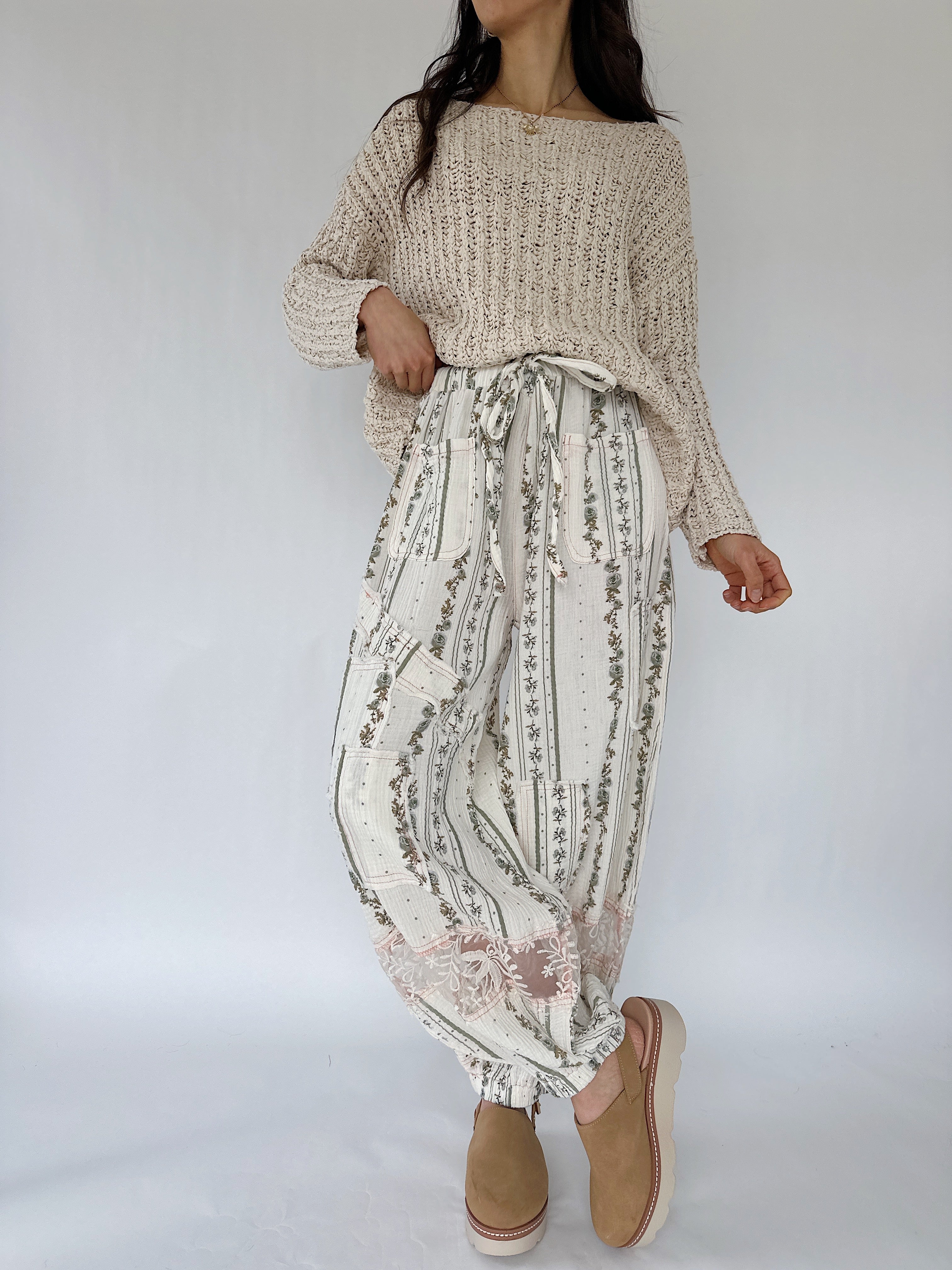 Person wearing a beige sweater and patterned pants on a white background