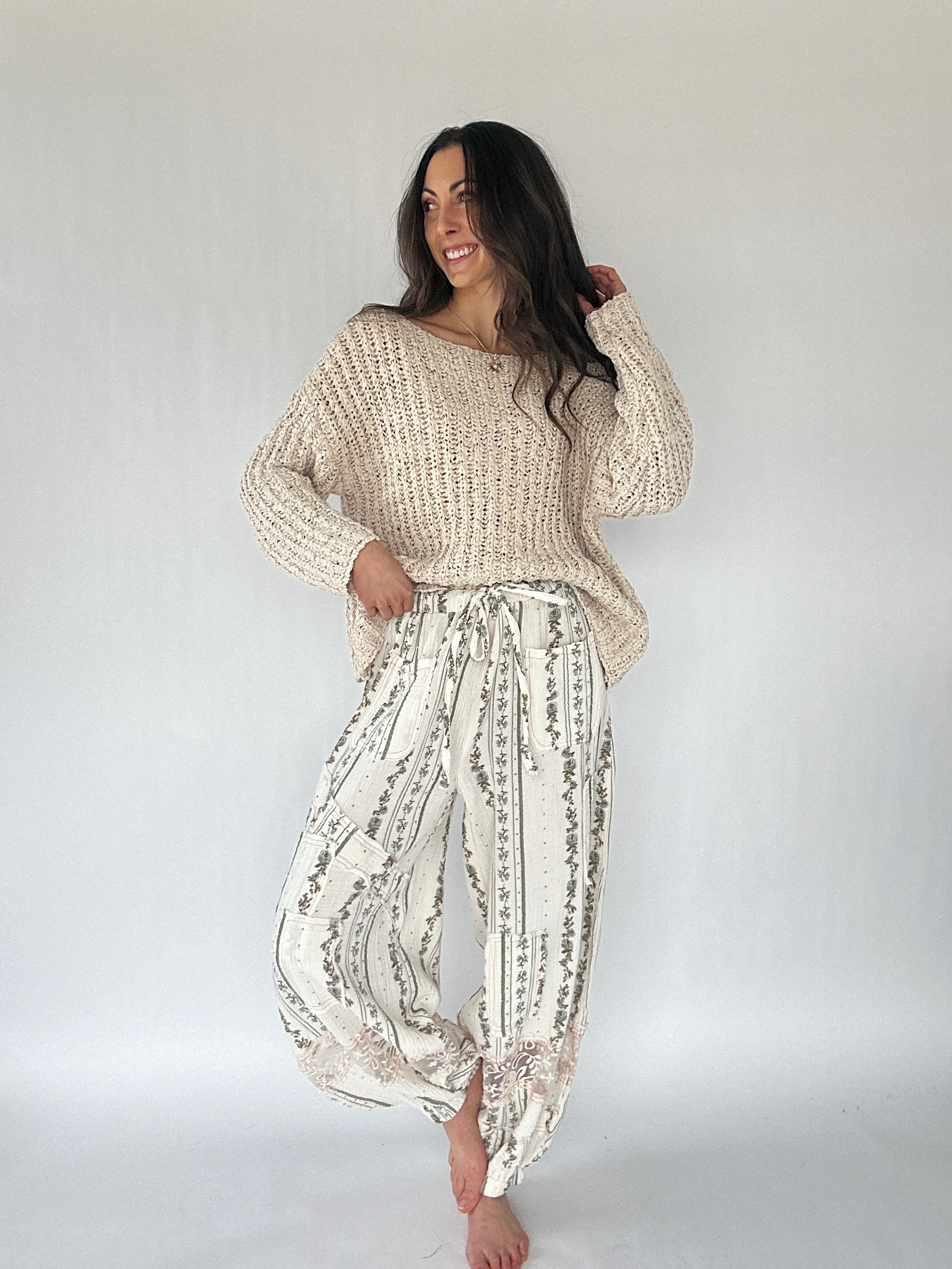 Woman wearing a beige knitted sweater and patterned pants on a white background