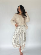 Woman wearing a beige knitted sweater and patterned pants on a white background