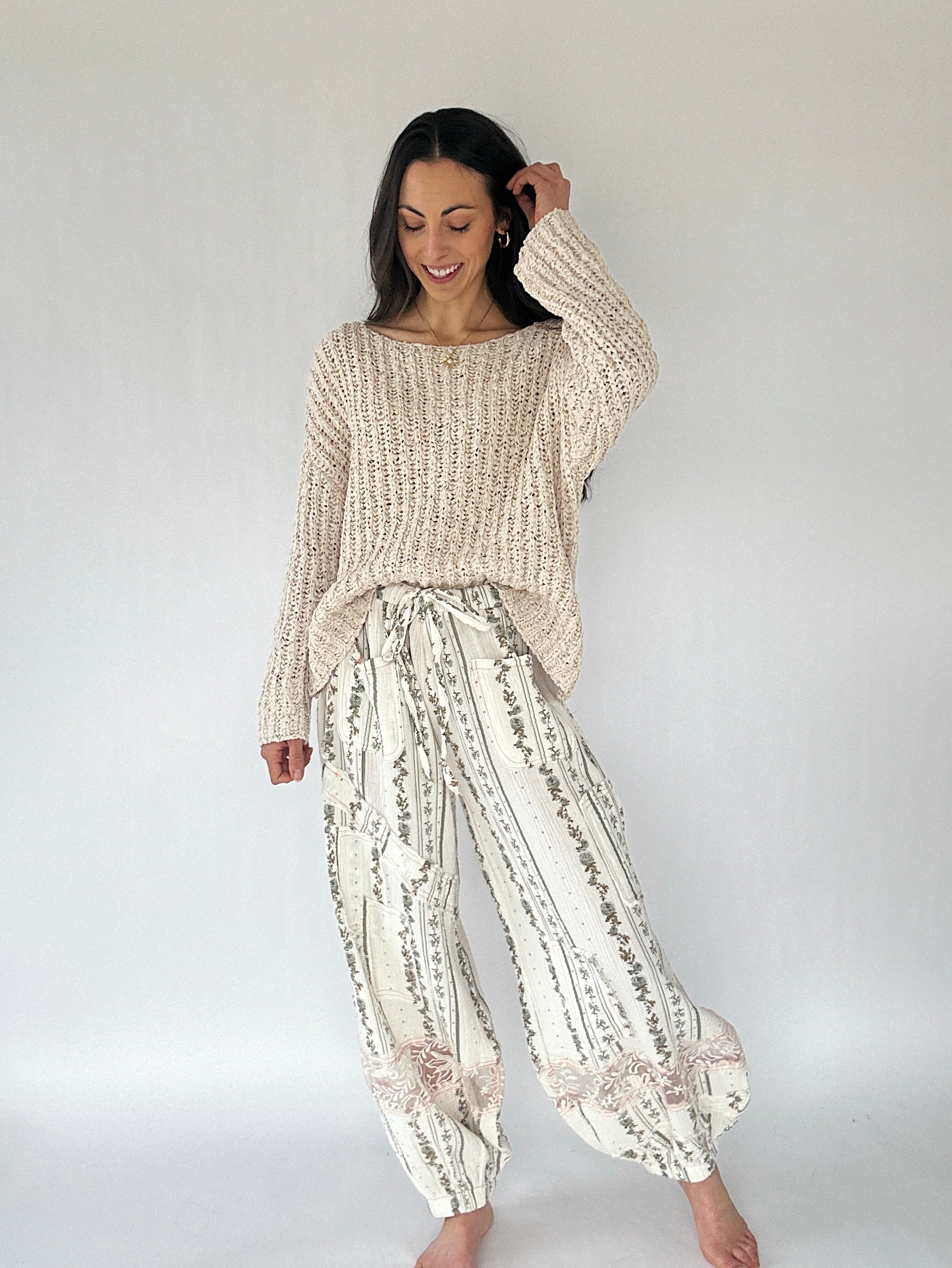 Woman wearing a beige knitted sweater and patterned pants against a white background