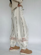 Person wearing white floral-patterned pants with brown shoes on a plain background