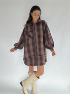 Woman wearing a plaid shirt dress with white boots on a plain background