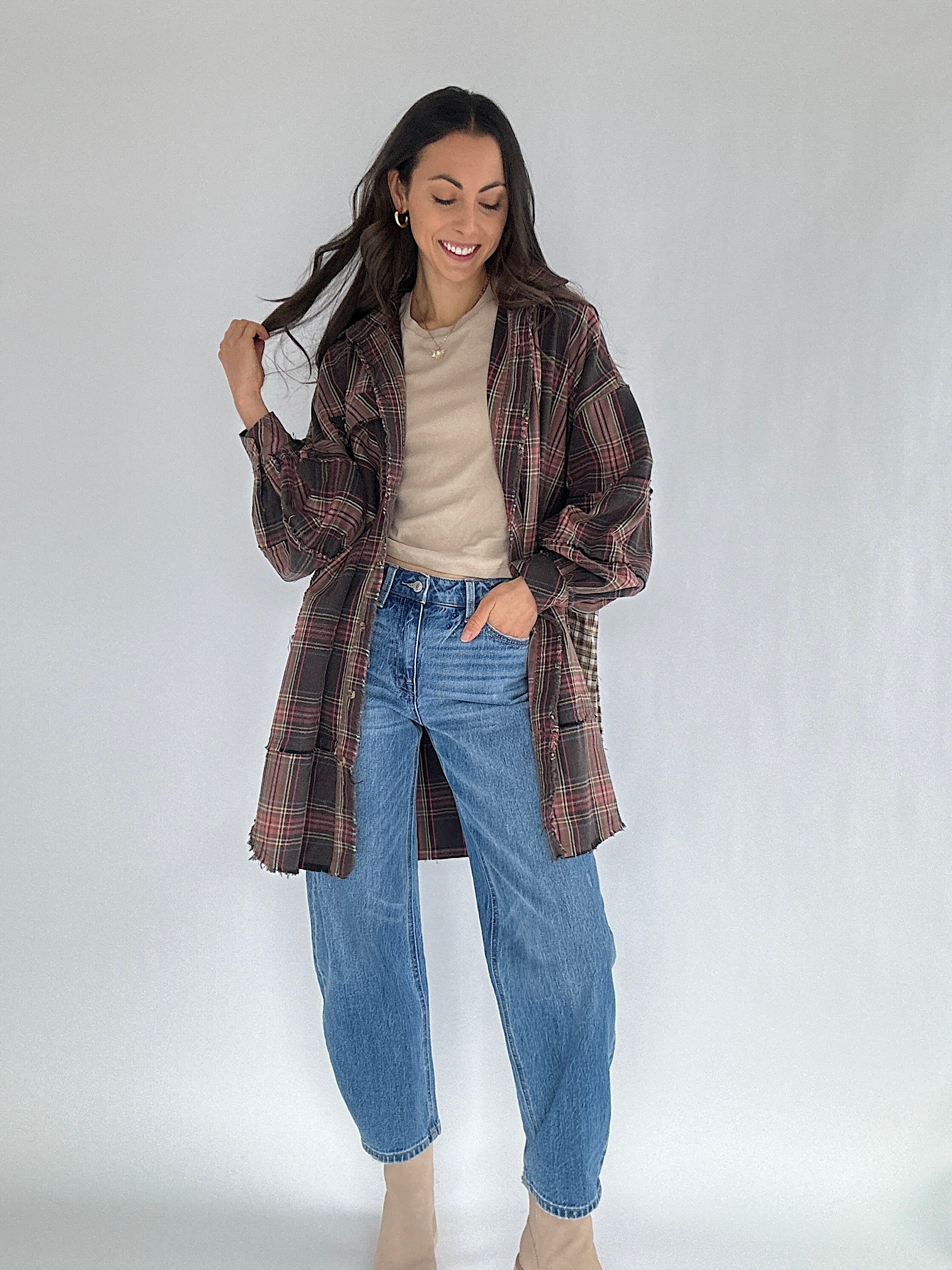 Woman wearing a plaid oversized shirt, beige tee, and blue jeans on a white background