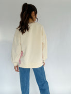 Person wearing a cream sweater and blue jeans against a white background