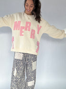 Person wearing a cream sweatshirt with 'MERRY' in pink and leopard patterned pants on a plain background