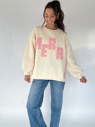 Woman wearing a cream sweatshirt with pink text and blue jeans on a white background