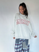 Woman wearing light grey mock neck pullover with "MERRY" embroidered lettering with plaid pants on a white background