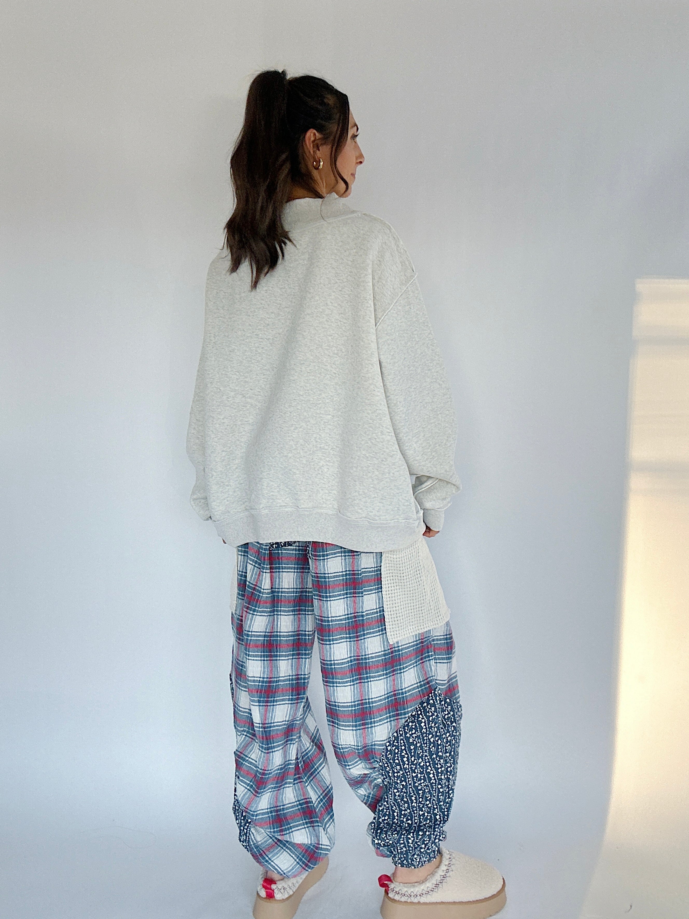Person wearing a light gray sweatshirt and plaid pants against a white wall back view