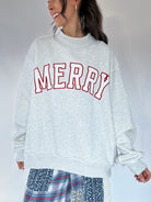 Person wearing a gray sweatshirt with 'MERRY' in red text on a plain background